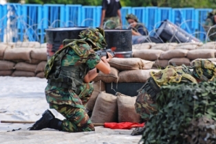 Photo of Airsoft game players hiding behind a fort made from bags stacked upon each other.