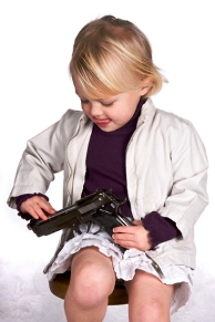 Picture of a little blond boy playing with a handgun in his lap.